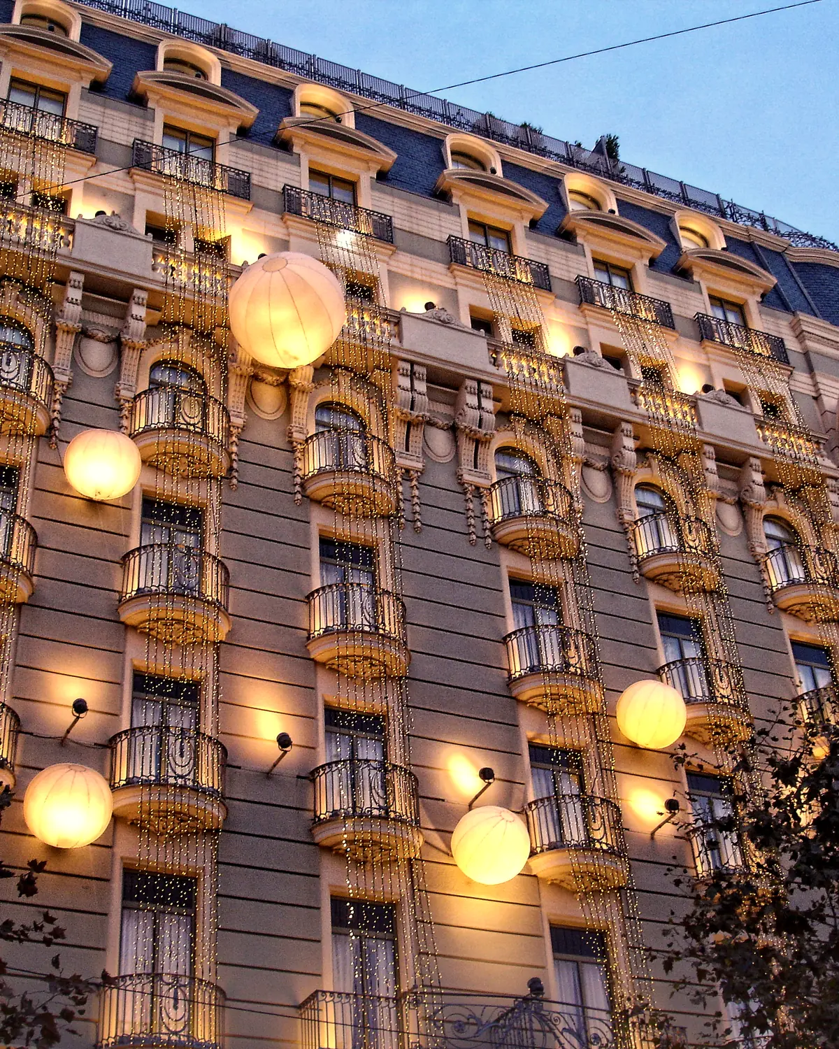 The hotel facade at dusk, with balconies, hanging lights and white globes against a blue sky