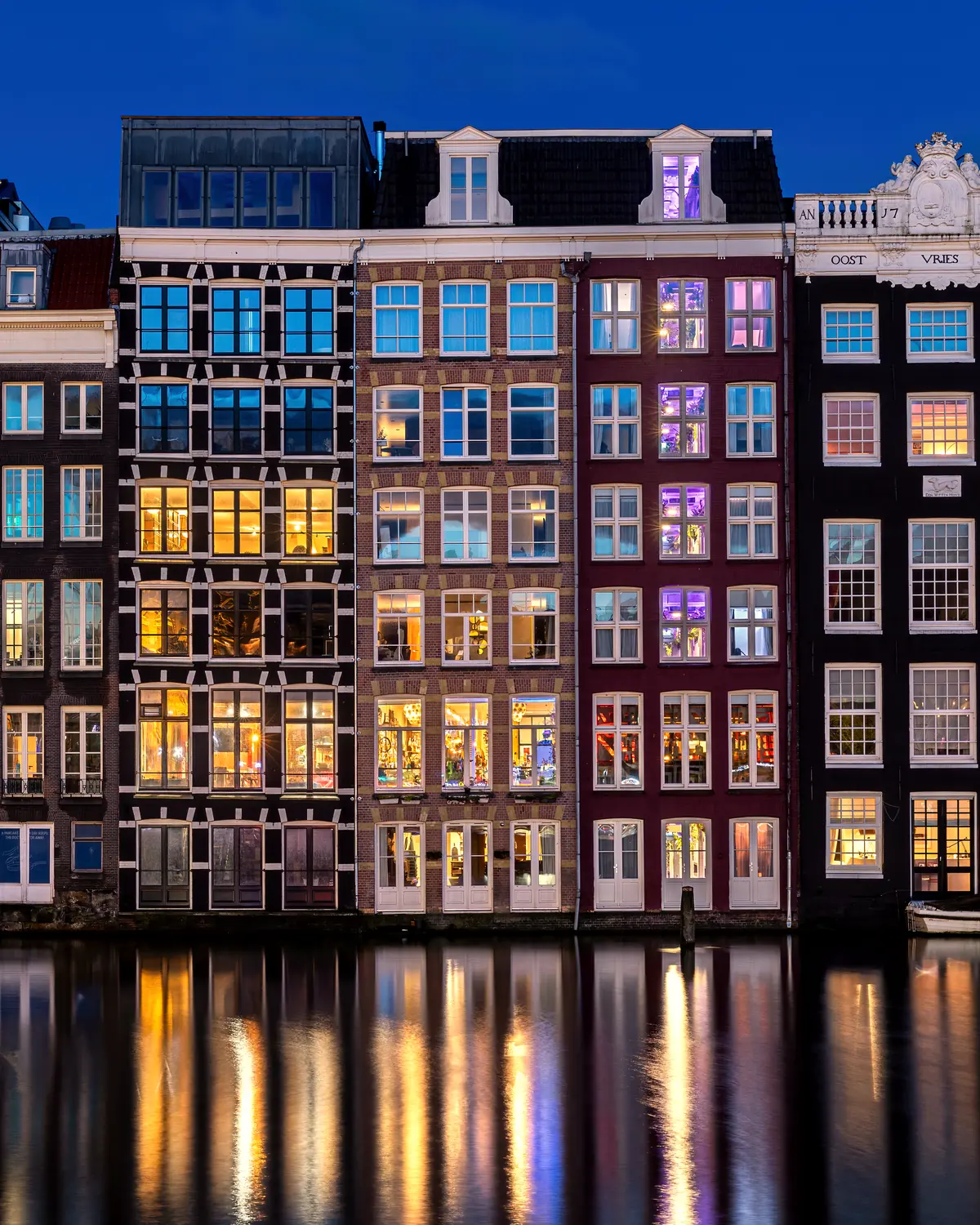 Water reflection of colorful windows of canal houses, east side, where the houses are located directly on the water, front view, at blue hour, in Damrak avenue, Amsterdam, Netherla