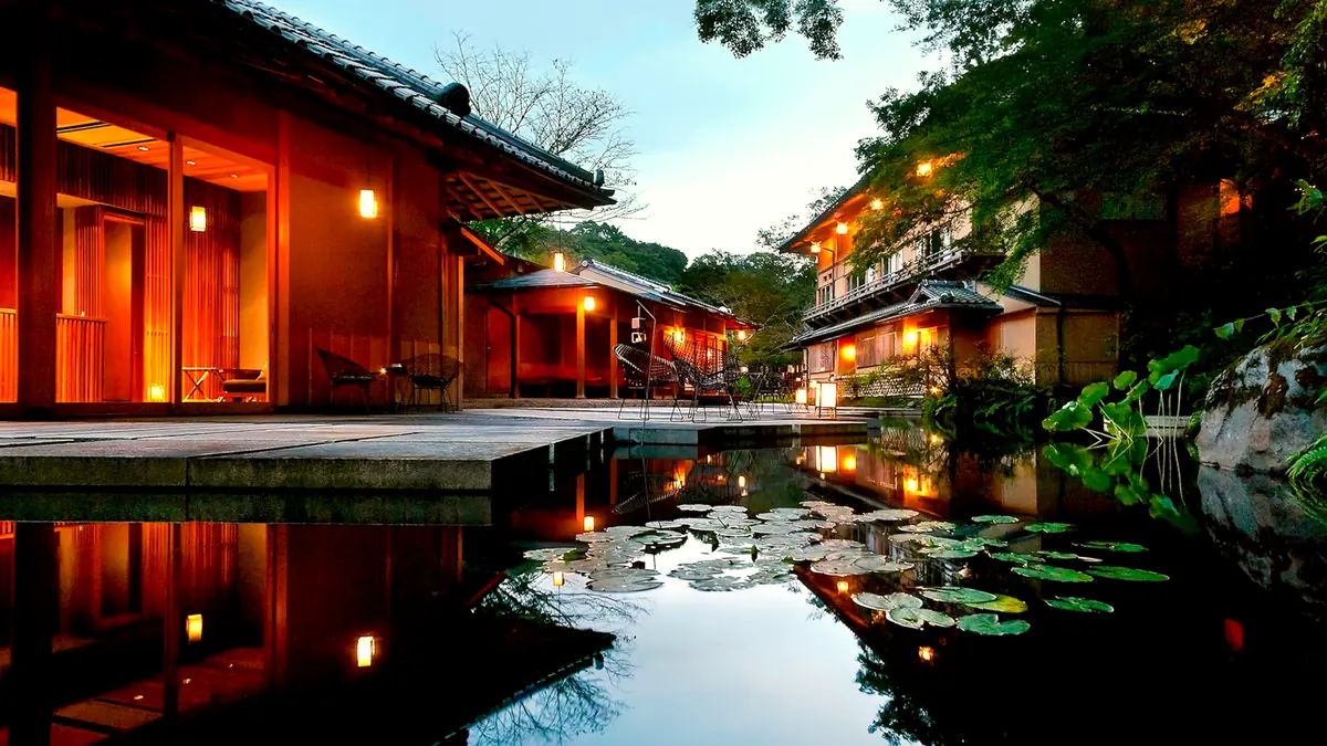 The water garden at Hoshinoya Kyoto at dusk: a pond with lily pads reflecting lit timber pavilions