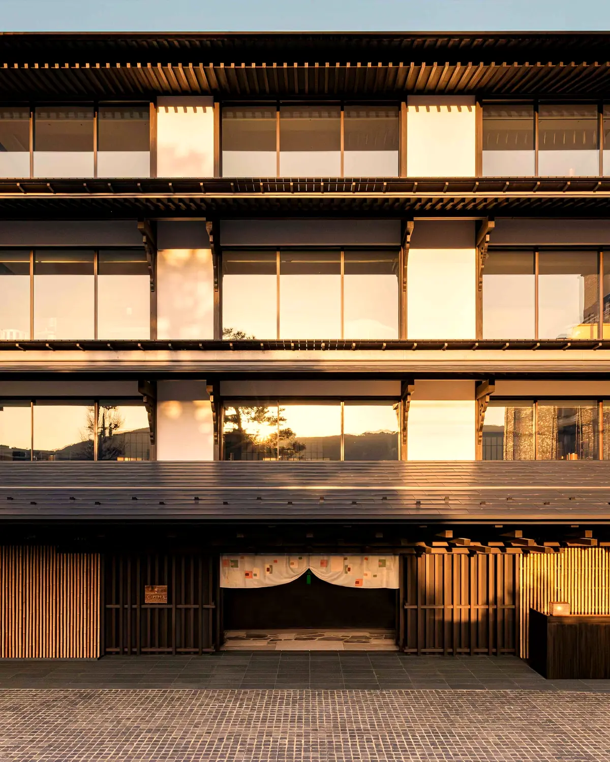 The street front of Capella Kyoto at dusk, with stacked eaves and a noren over the entrance