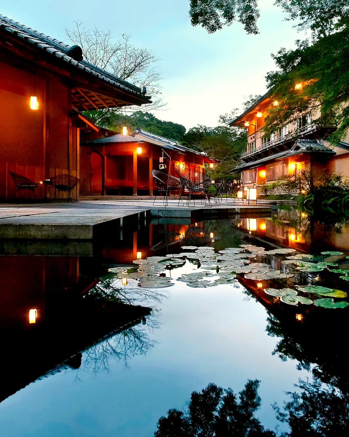The 'water garden' at dusk: a pond with lily pads reflecting the lit timber pavilions and guest buildings (caption: 歴史ある意匠と革新的なデザインが融合した「水の庭」)