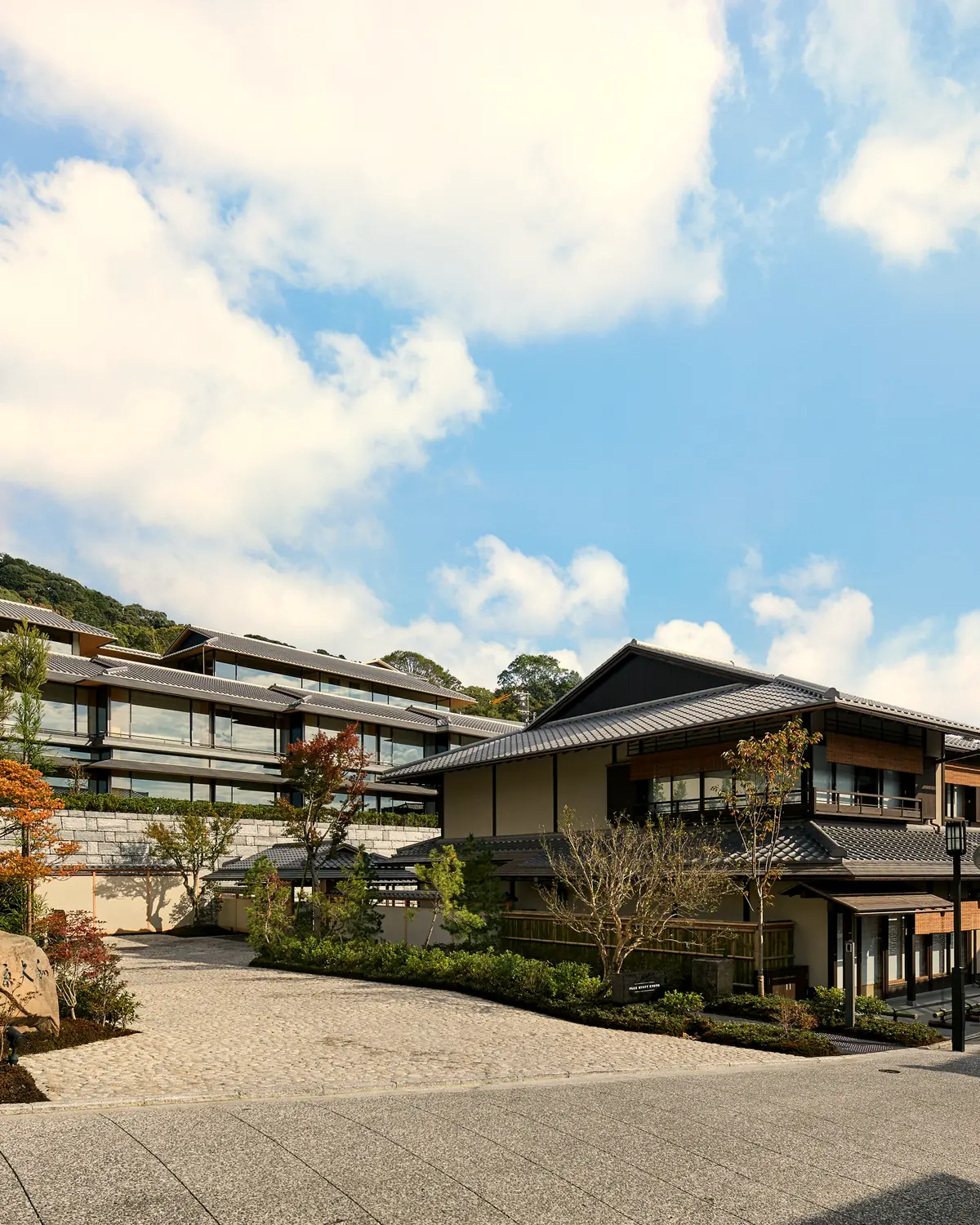 The hotel's low-rise buildings with tiled roofs on the hillside beside the stone-paved Ninenzaka lane, with a stone lantern and garden in the foreground