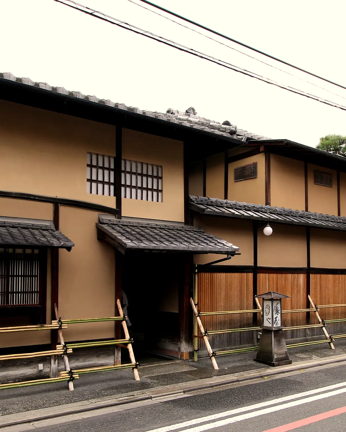 The street frontage of Tawaraya Ryokan: plastered walls, tiled eaves, bamboo inuyarai fences and the entrance with a stone lantern sign