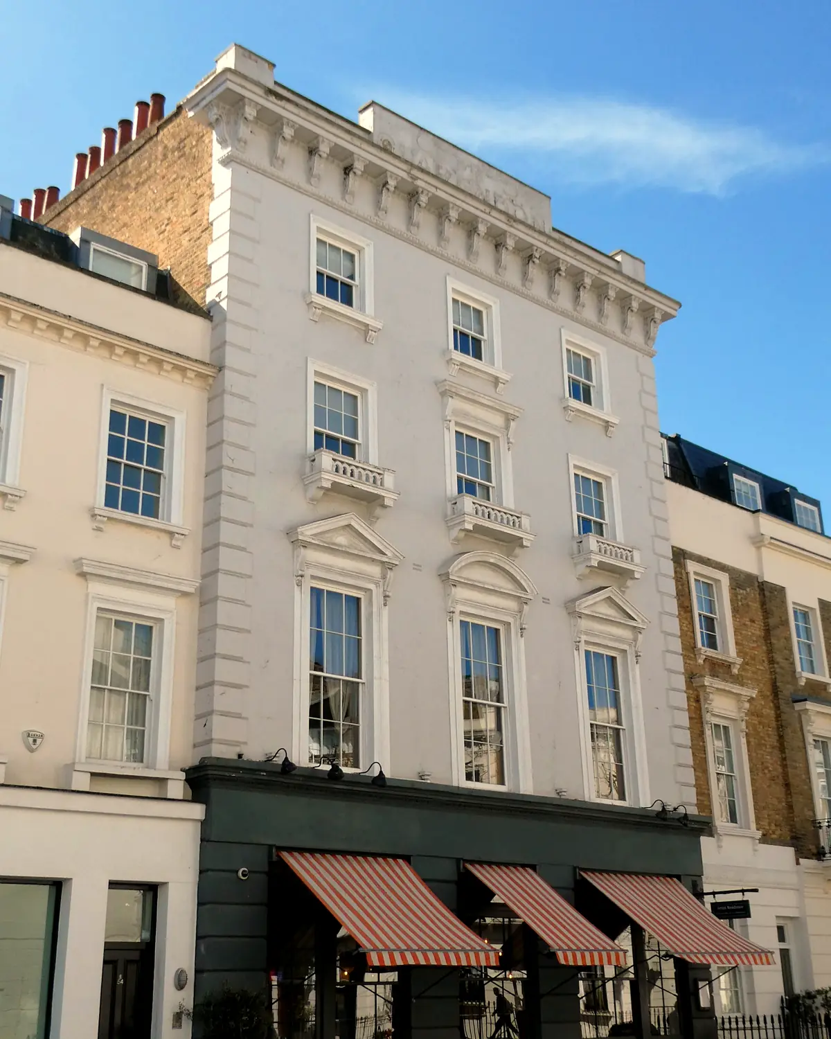 White stucco facade of Artist Residence on Cambridge Street, Pimlico, with striped awnings over the restaurant