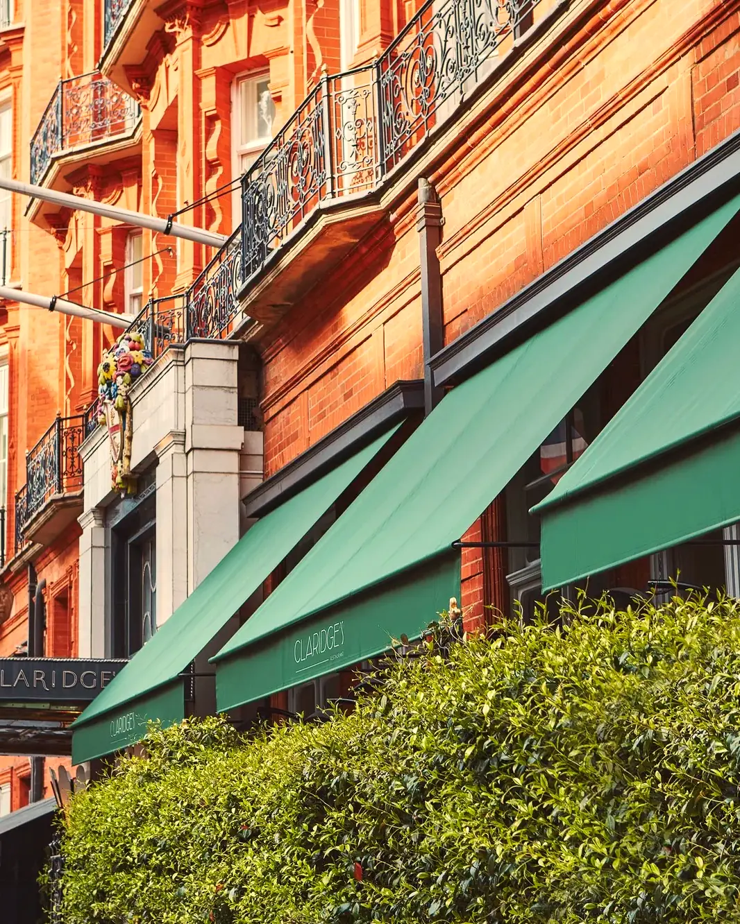 Red-brick facade with green awnings bearing the Claridge's name, Union flag and hedged terrace (from the release on Claridge's Restaurant terrace)