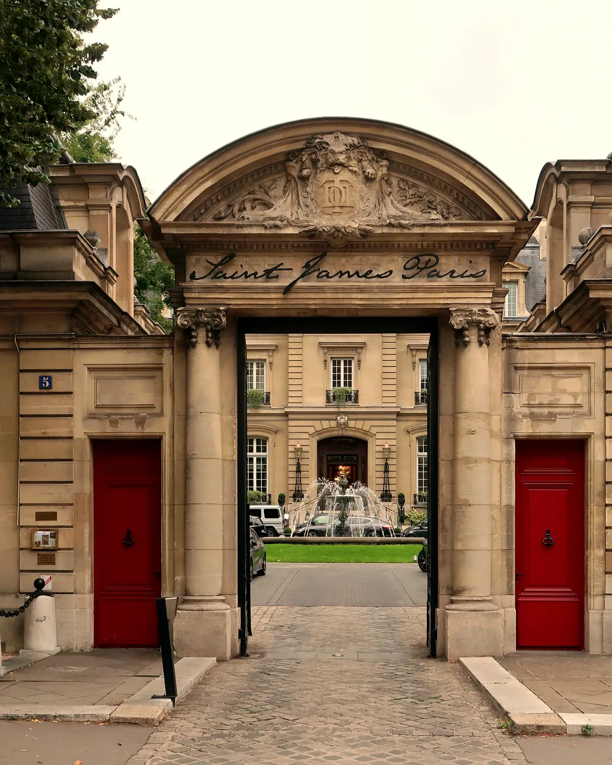 Exterior: the carved stone entrance gateway lettered 'Saint James Paris' at 5 place du Chancelier-Adenauer, with the courtyard fountain and main house beyond