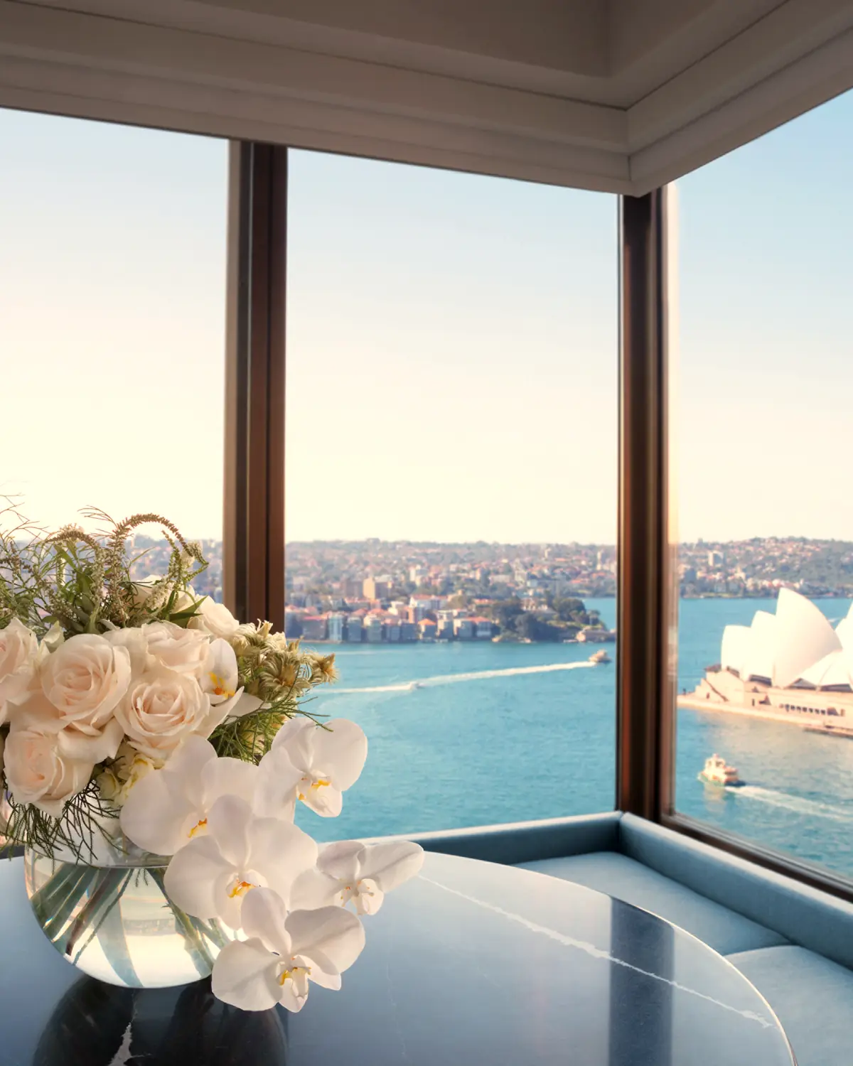Corner guest room window looking over Circular Quay to the Opera House and Harbour Bridge, table with white flowers in the foreground