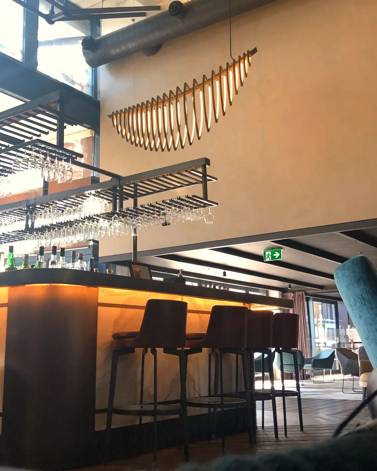 The lobby bar: a marble-fronted counter, hanging wine glasses and a boat-shaped light over the double-height room