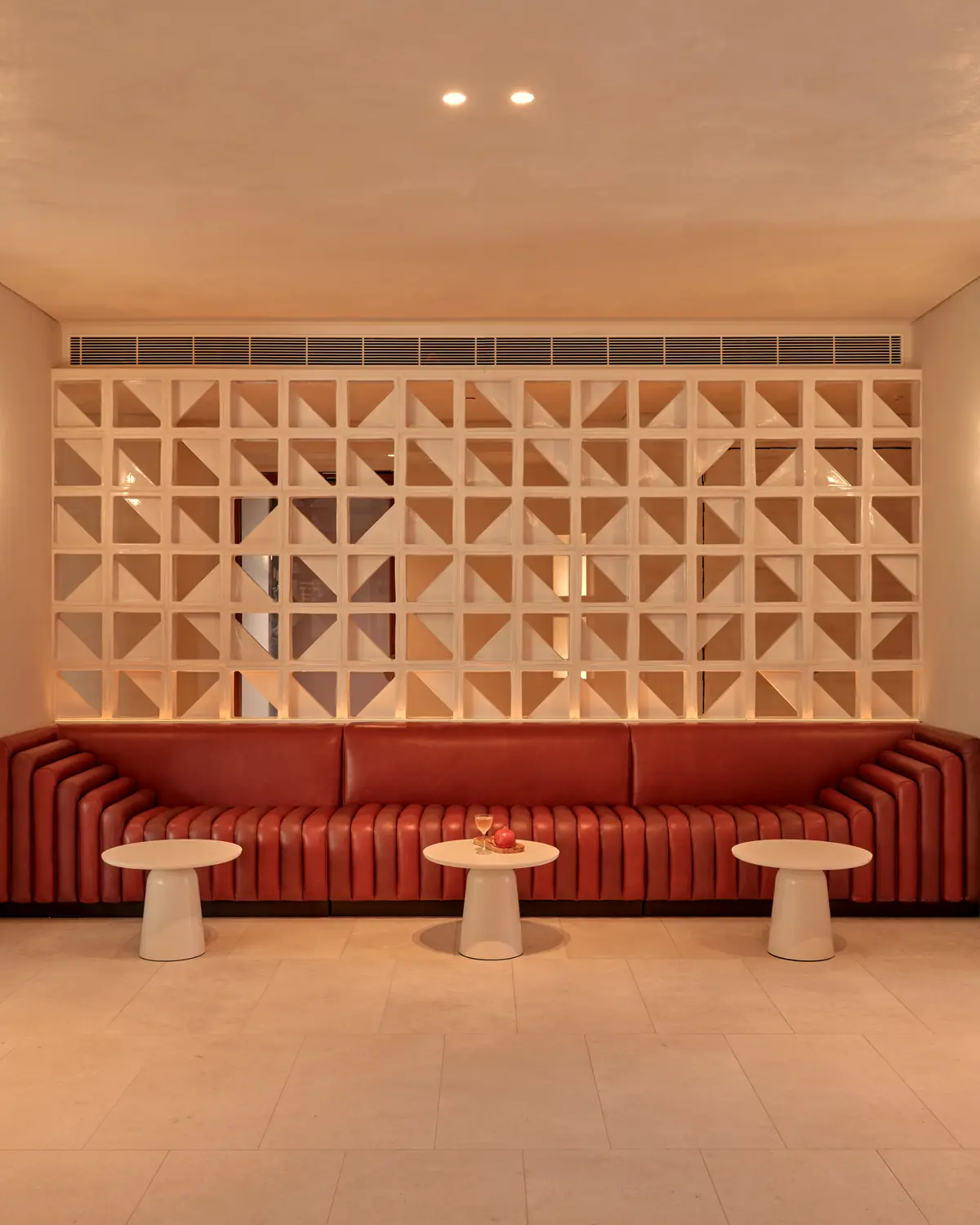 Lobby seating: red banquette in front of a white breeze-block screen between two curved columns (gallery file "the-eve-hotel-sydney-lobby-06-2025")