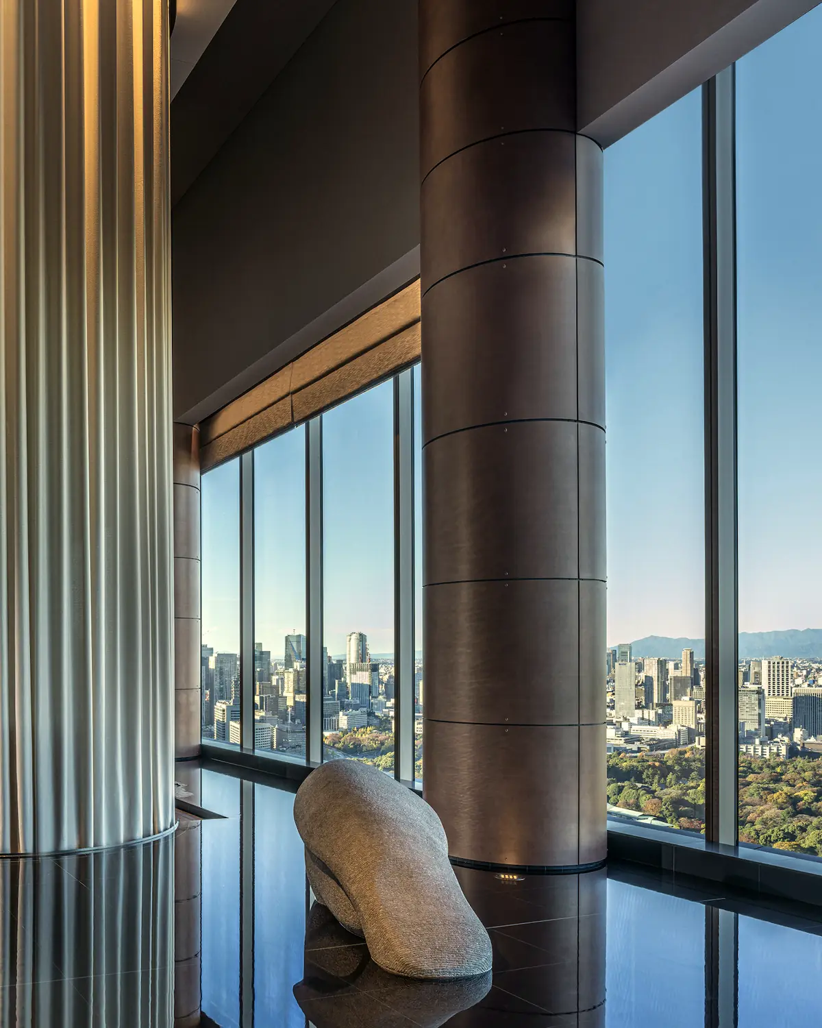 The arrival level at Four Seasons Hotel Tokyo at Otemachi: a fluted silver column, a stone sculpture, and windows over the Imperial Palace gardens to Mount Fuji