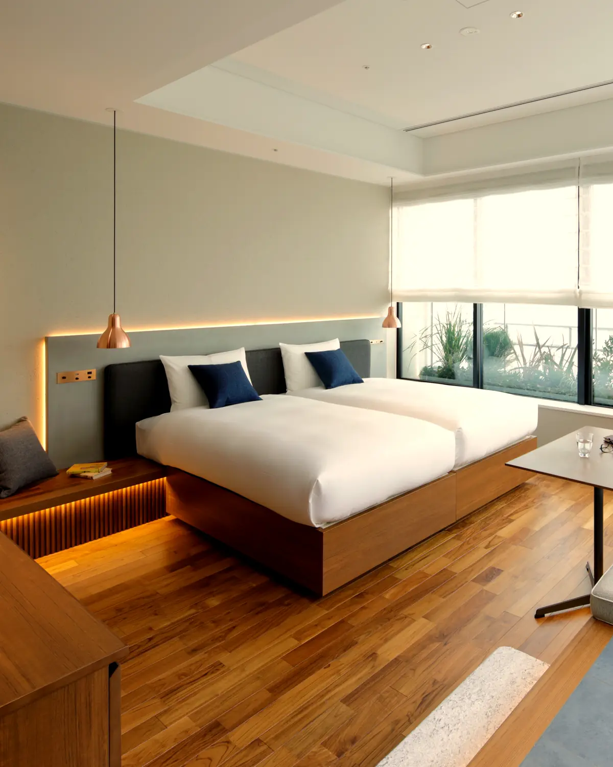 A guest room at Hamacho Hotel Tokyo: twin beds, a timber platform, and a planted terrace window