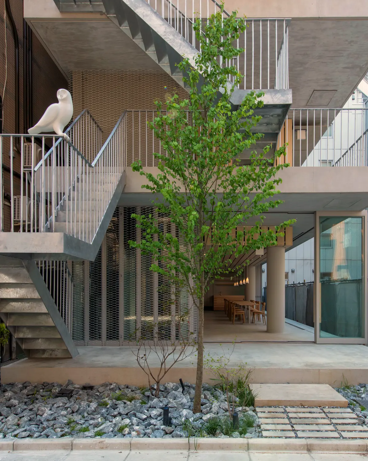 The street courtyard at Hotel Siro: an open stair, a young tree, and a white owl on the railing