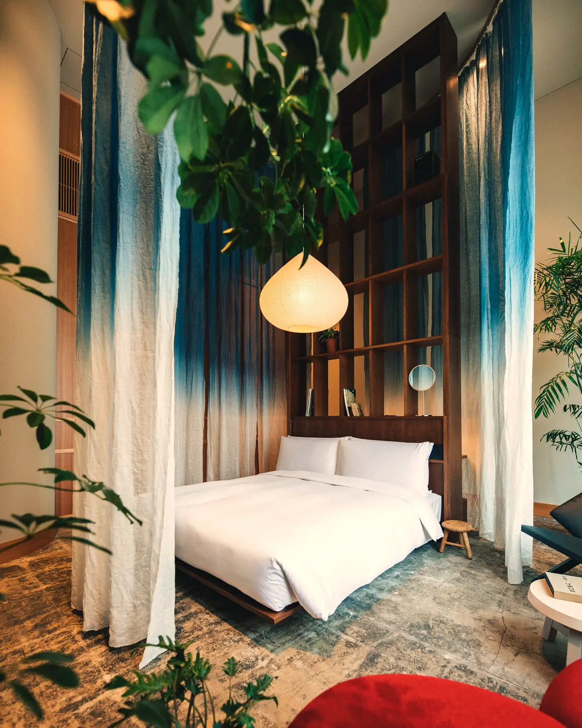 A guest room at K5: a timber bed behind indigo-dyed linen, a paper lantern, and a lattice shelf